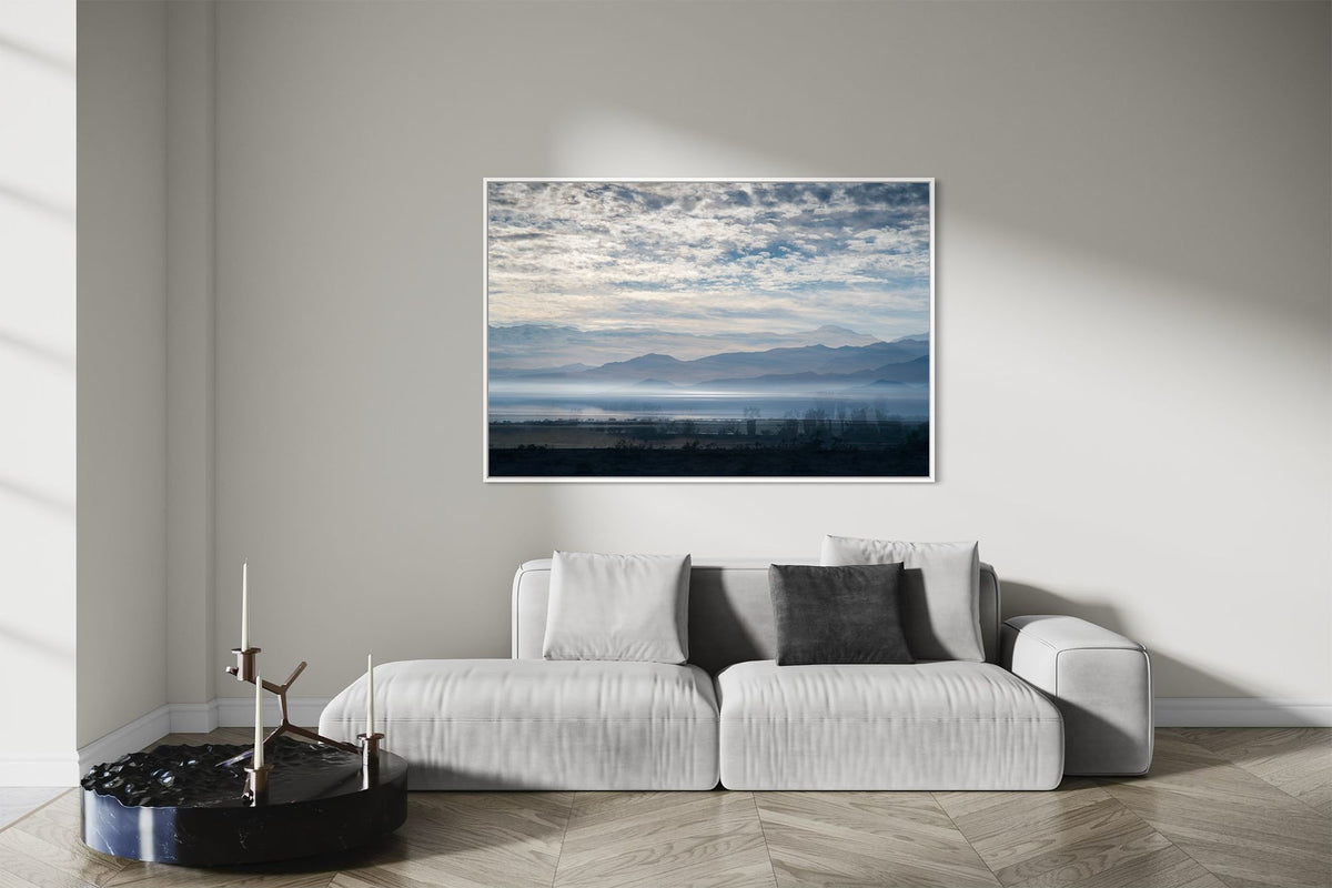 Blue Salton Sea layered photography print in a white floater frame, displayed above a light gray sofa in a modern living room